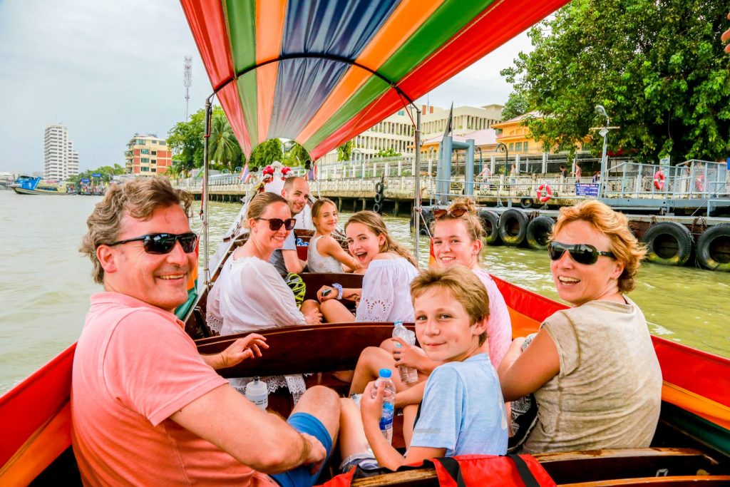 Group of eight tourists, some children, looking back and smiling on boat in the canals of Bangkok