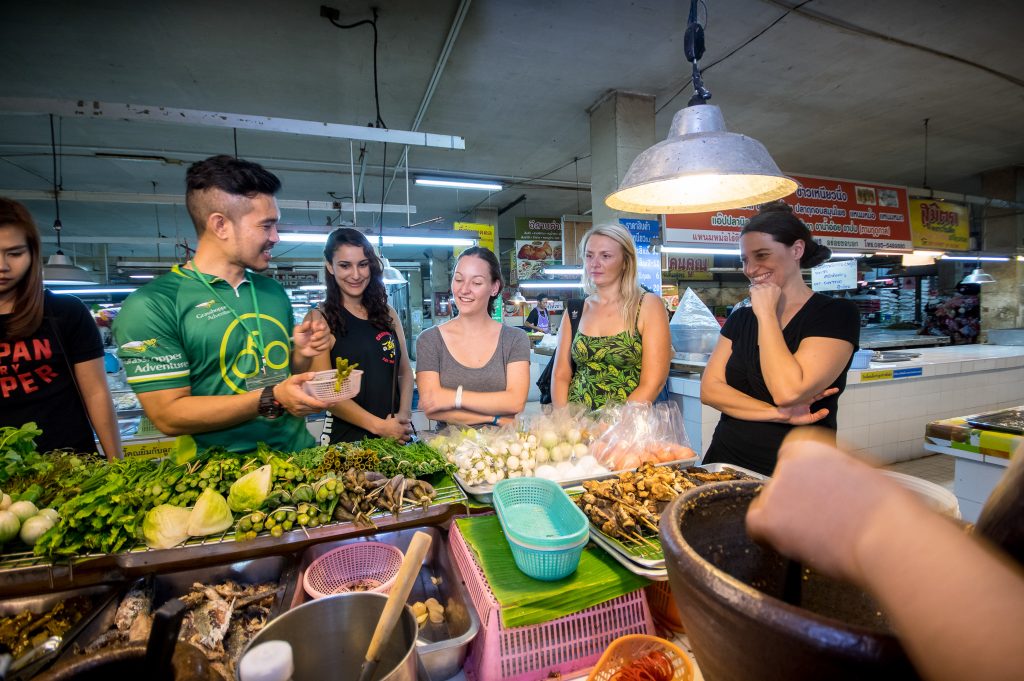 Guide talking to four women about local fresh vegetables at stand in Chiang Mai