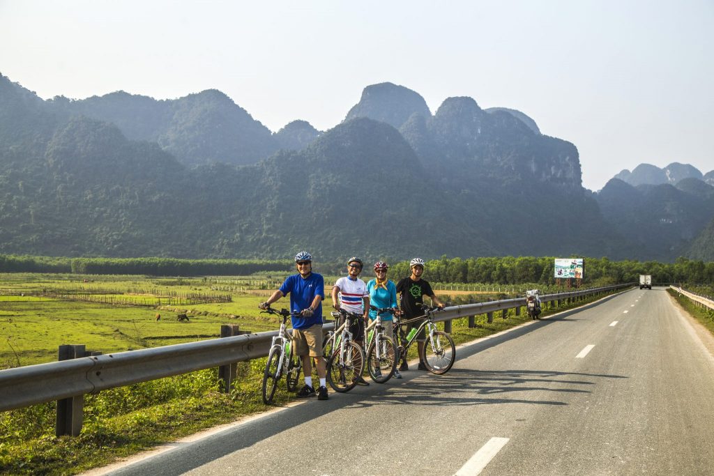 Four cyclists stopped by side of the road in front of limestone karsts in Vietnam