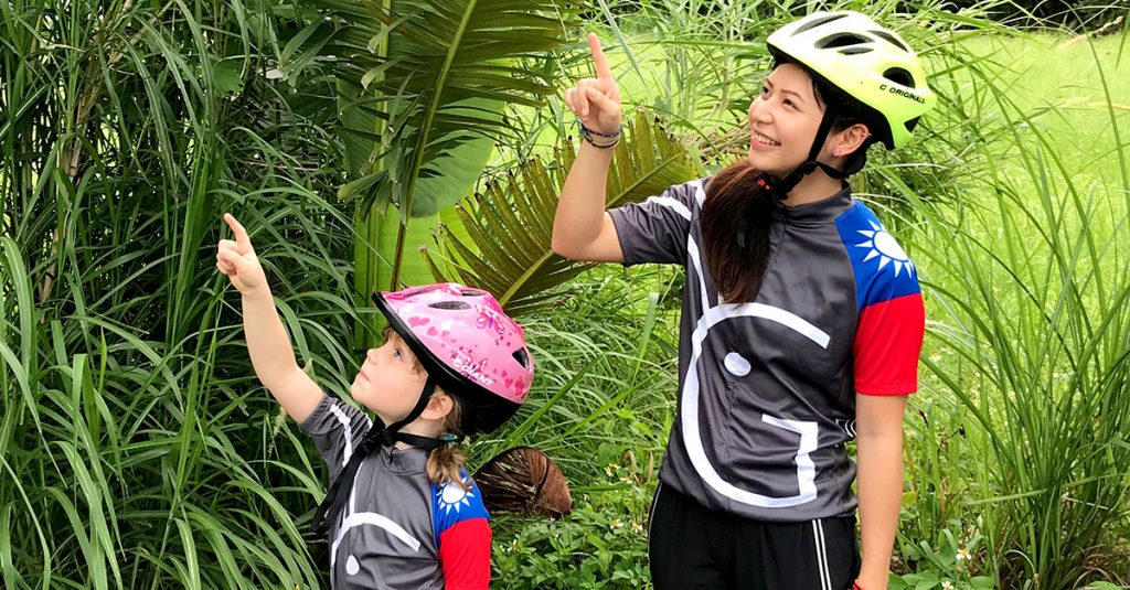 Woman and young girl in Grasshopper Adventures Taiwan cycling jerseys pointing at palm fronds