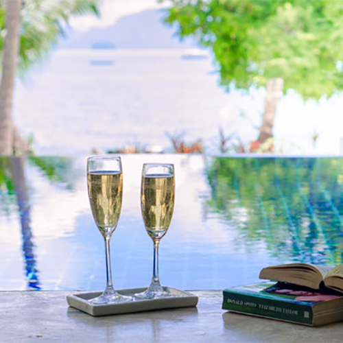two champagne glasses overlooking pool and ocean in background
