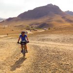 Female cyclist riding through steppe with hill behind