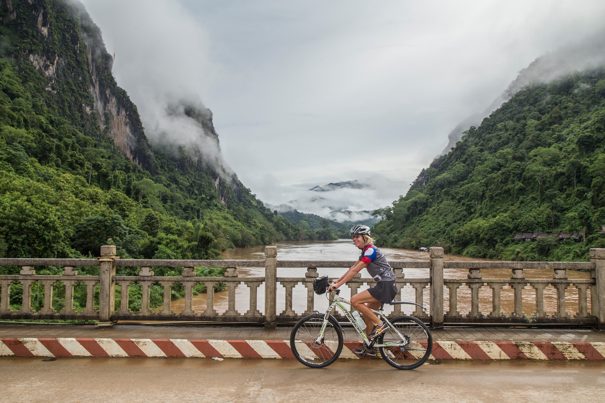 Cyclist crossing bridge with misty mountains of Laos behind