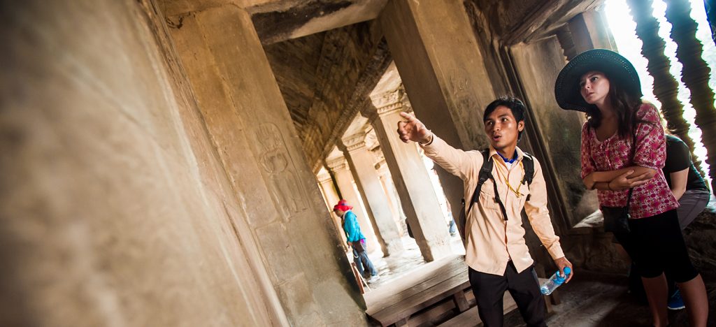 Cambodian guide pointing out walls of Angkor Wat to traveler