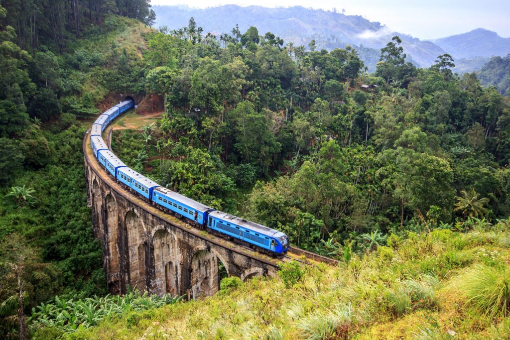 Blue train on curved bridge through hill country of Sri Lanka