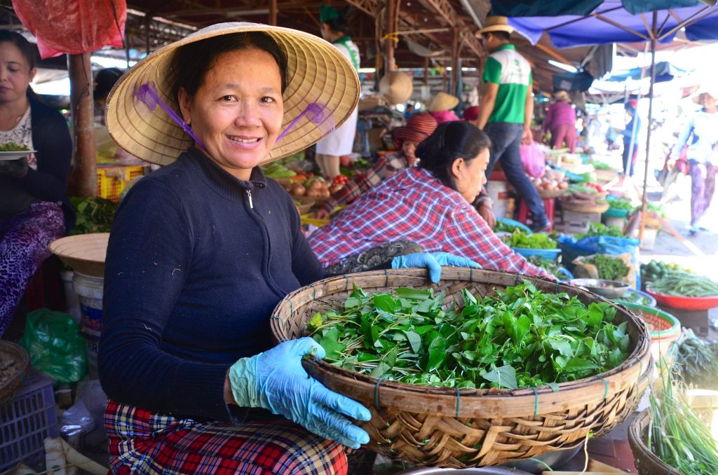 Vietnamese market lady holding a basket of herbs