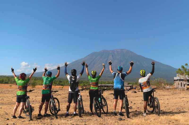 Cyclists in the Savannah area of Bali looking at Mount Agung